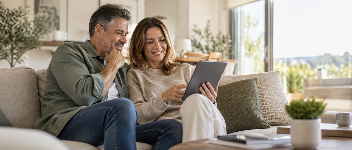 Pareja consultando el valor de su vivienda en una tableta desde el sofá de su casa